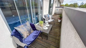 A balcony with a wicker sofa, a small table with two cups, and a potted plant.