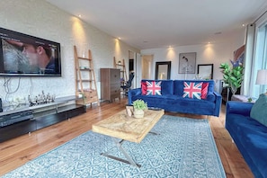 A living room with a blue sofa, wooden coffee table, and a flat-screen TV mounted on the wall. - 3bdr Penthouse W/ Balcony | islington, kings cross (London)