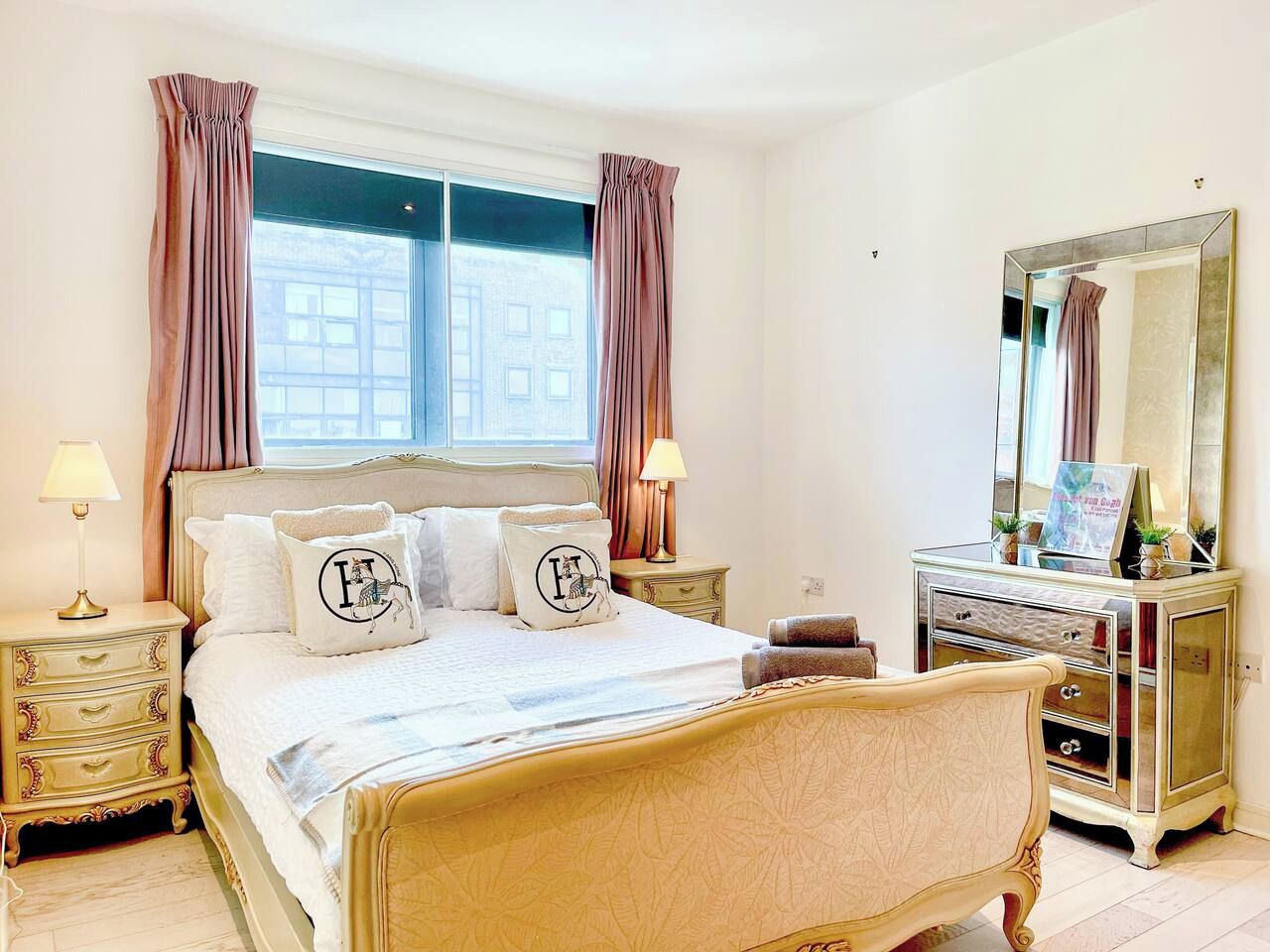 A bedroom with a large bed, bedside tables, a dresser, a mirror, and a window with curtains.