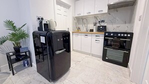 Une cuisine moderne avec des armoires blanches, un réfrigérateur noir, un four encastré et un pare-feu en marbre.