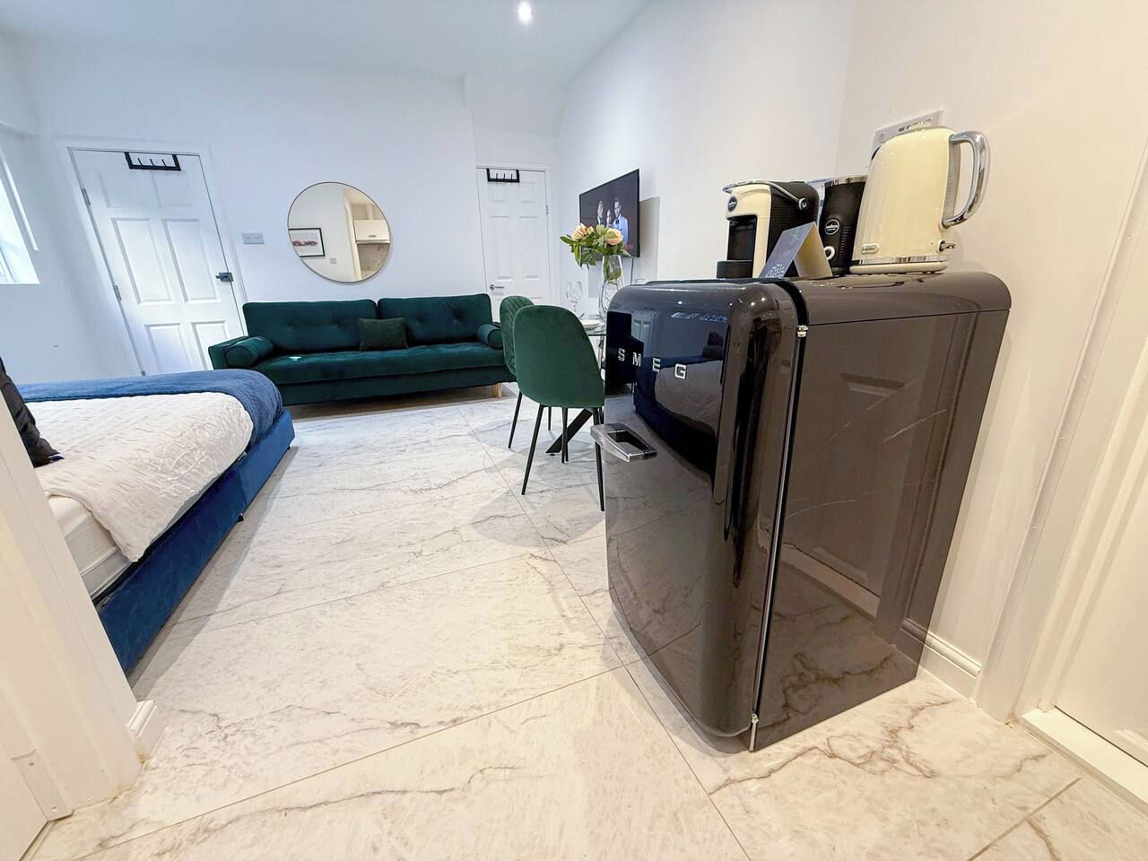 En kompakt opholdsstue med en seng, en grøn sofa, et lille spisebord og et køleskab.