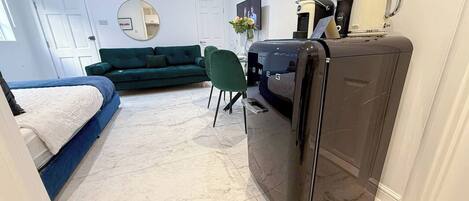 A compact living space with a bed, a green sofa, a small dining table, and a refrigerator.