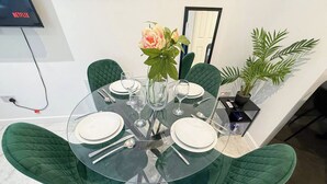 Une table ronde en verre, quatre chaises, un vase avec des fleurs et une plante en pot, le tout posé sur un sol blanc.