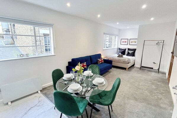 A modern living room with a dining area, a blue sofa, and a glass table set for four.