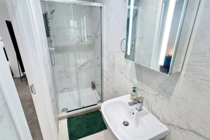 A modern bathroom with a glass-enclosed shower, a white sink, and a mirror above it.