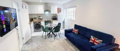 A compact living space with a dining area, a sofa with a Union Jack pillow, and a TV mounted on the wall.