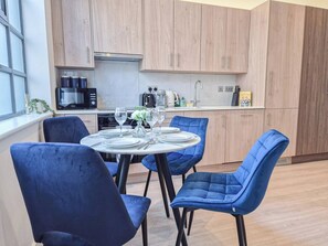 A modern kitchen with wooden cabinets, a dining table set for four, and blue chairs.