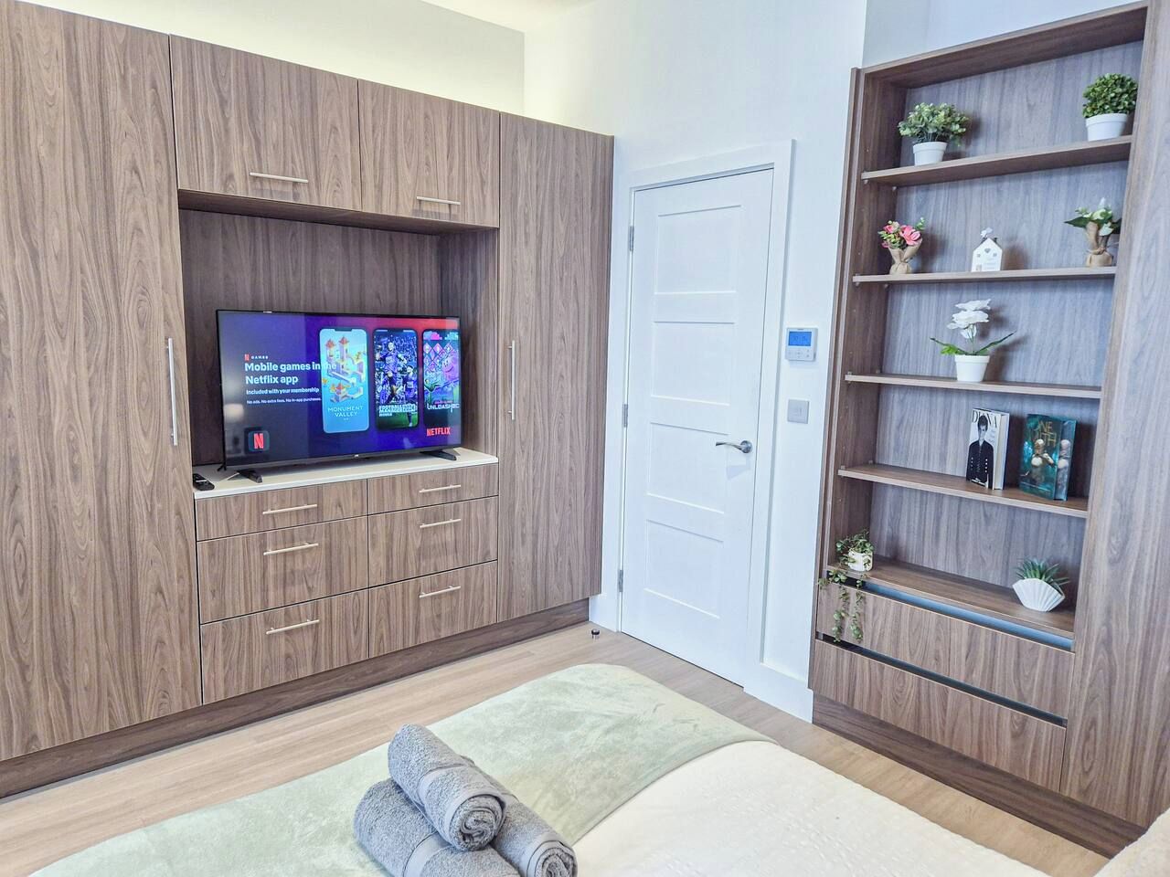 A modern room with a flat-screen TV mounted on a wooden cabinet, a white door, and a wooden shelving unit with decorative items.
