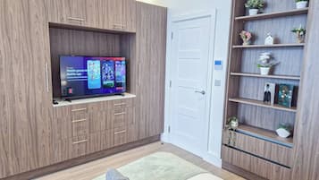 A modern room with a flat-screen TV mounted on a wooden cabinet, a white door, and a wooden shelving unit with decorative items.