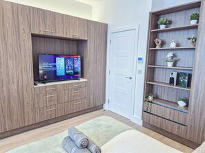 A modern room with a flat-screen TV mounted on a wooden cabinet, a white door, and a wooden shelving unit with decorative items.