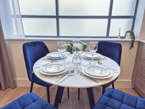 A dining table set for four with chairs, a window with blinds, and a plant on the windowsill.