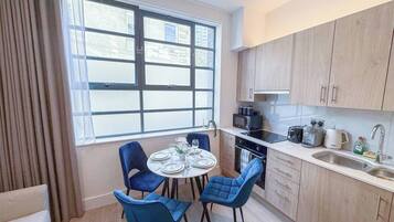 A compact kitchen with a dining area, featuring a round table with chairs, a window with blinds, and modern appliances.