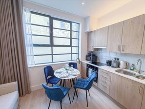 A compact kitchen with a dining area, featuring a round table with chairs, a window with blinds, and modern appliances.