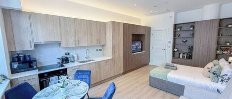 A modern apartment with a dining area, kitchenette, and a living space with a sofa and TV.
