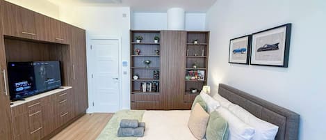 A modern bedroom with a bed, a television, a wardrobe, and a bookshelf.