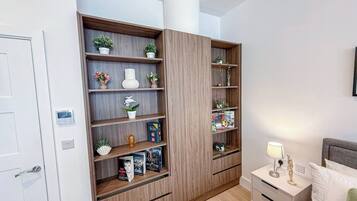 A bedroom with a built-in wooden shelving unit, a bedside table with a lamp, and a bed with pillows.