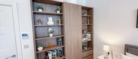 A bedroom with a built-in wooden shelving unit, a bedside table with a lamp, and a bed with pillows.