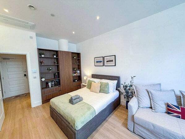 A bedroom with a bed, a sofa, a bookshelf, and a door.