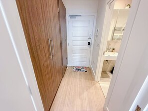 A narrow hallway with a wooden wardrobe, a white door, and a glimpse of a bathroom with a sink and mirror. - Chic studio flat in Regent's Park near Marylebone (London)