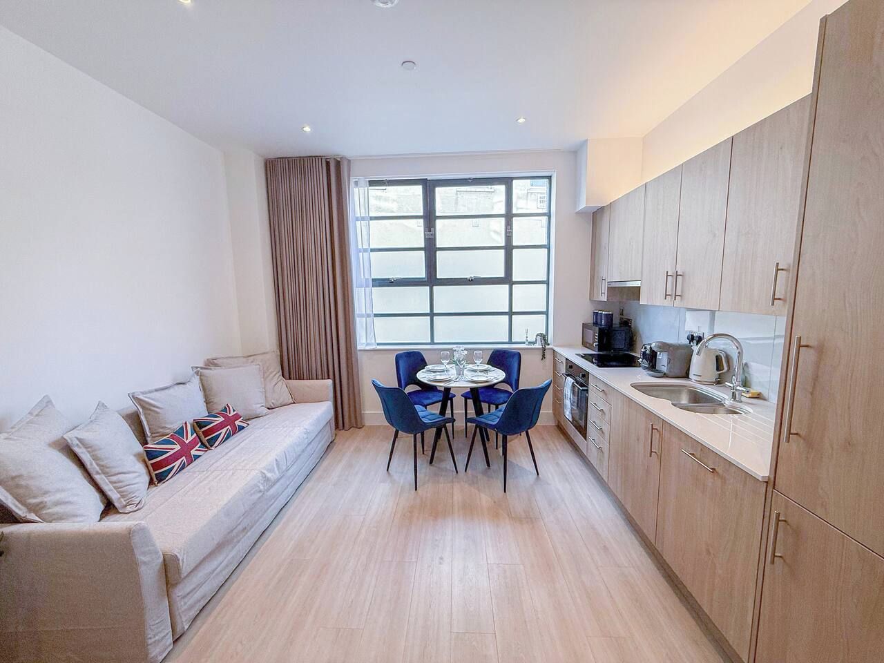 A compact living space with a sofa, a dining table with chairs, a kitchen area, and a large window providing natural light.