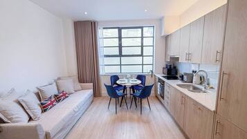 A compact living space with a sofa, a dining table with chairs, a kitchen area, and a large window providing natural light.