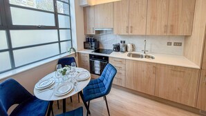 A modern kitchen with wooden cabinets, a dining table set for four, and a large window offering a view of the city. - Chic studio flat in Regent's Park near Marylebone (London)