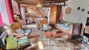 Un accogliente soggiorno con divano, poltrone e tavolino. Una scala conduce a una cucina sullo sfondo.