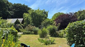Un giardino con due sedie blu, un prato verdeggiante e diverse piante e alberi.