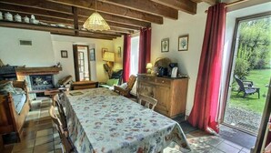 Una stanza accogliente con camino, mobili in legno, un tavolo da pranzo con tovaglia floreale e vista sul giardino attraverso un'ampia finestra.