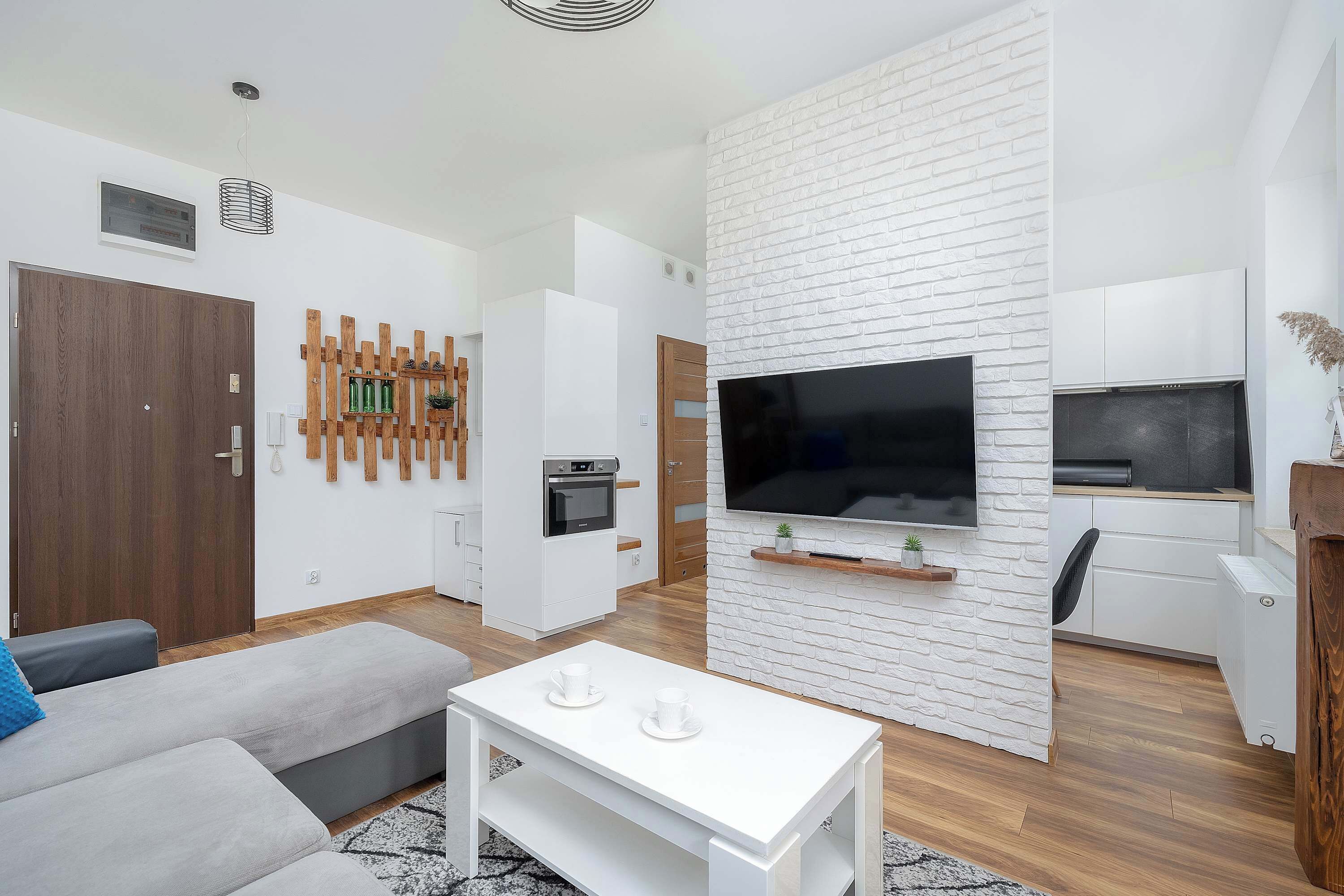A modern living room with a sofa, a coffee table, a TV, and a kitchen area with a microwave and oven.