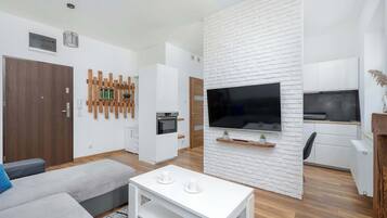 A modern living room with a sofa, a coffee table, a TV, and a kitchen area with a microwave and oven.