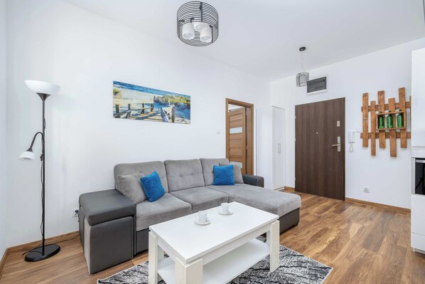 Una sala de estar moderna con un sofá seccional gris, una mesa de centro blanca, una lámpara de pie y un cuadro con una escena de playa.