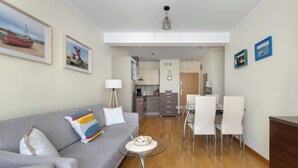 A modern living room with a grey sofa, a glass coffee table, and a dining area with white chairs and a small table.