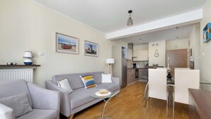 A modern living room with a grey sofa, a glass coffee table, and a dining area with white chairs.