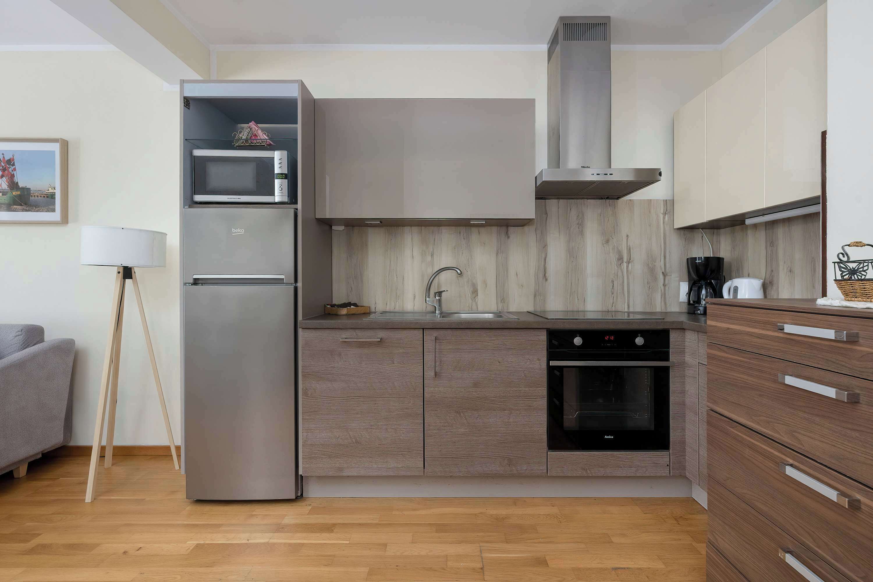 Una cocina compacta con microondas, horno y pileta integrados, muebles de madera y un diseño moderno.