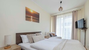 A hotel room with two beds, a television, a nightstand, a lamp, and a painting of a sunset.