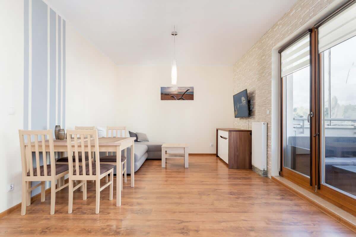 Ein modernes Wohnzimmer mit einem Holzesstisch, Stühlen, einer Couch und einem an der Wand befestigten Fernseher.