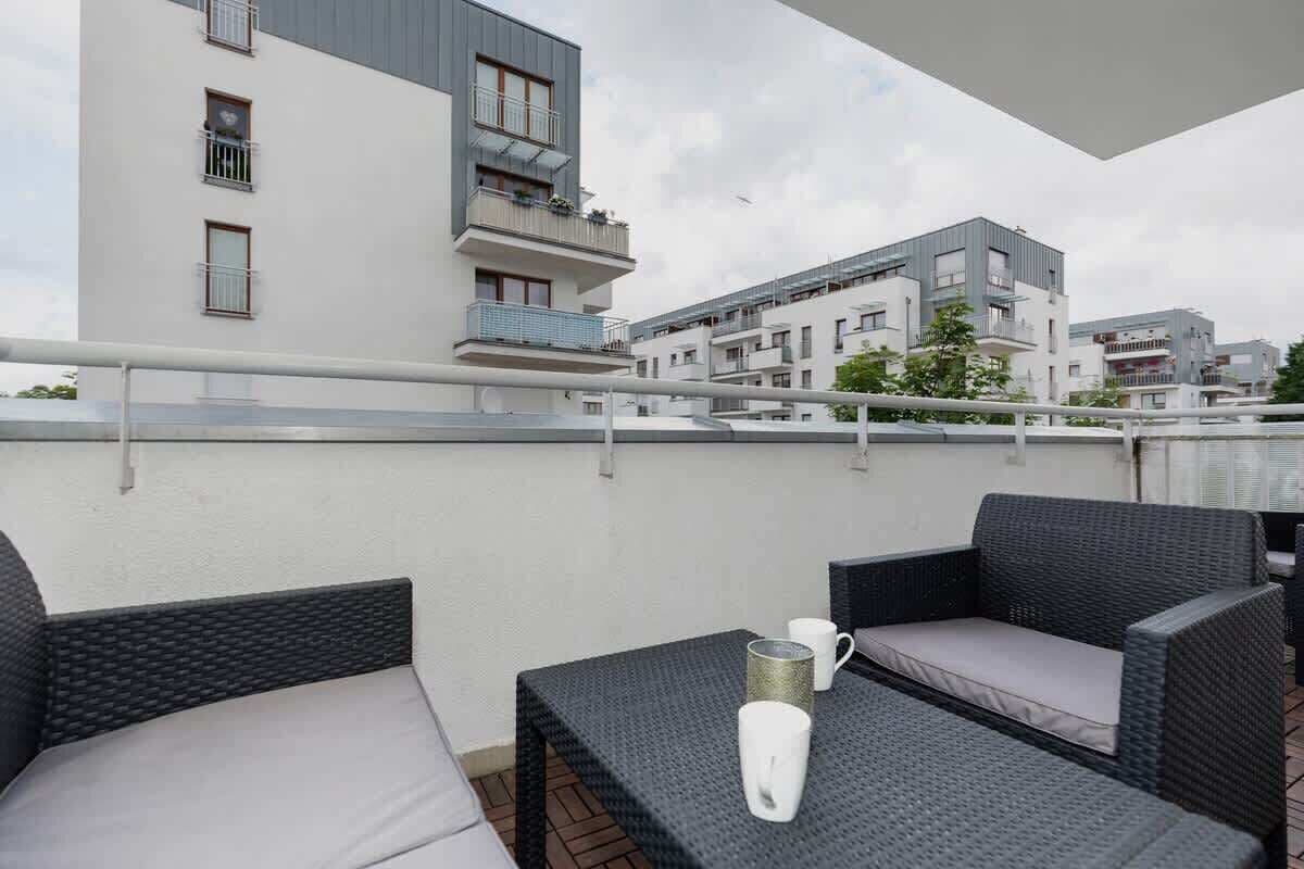 Un balcón con mobiliario de mimbre, una taza blanca y vistas de edificios modernos.