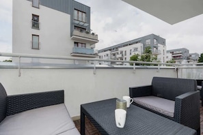 Ein Balkon mit Korbmöbeln, einer weißen Tasse und Blick auf moderne Gebäude.