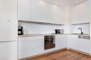 A modern kitchen with white cabinetry, stainless steel appliances, and a wooden countertop.