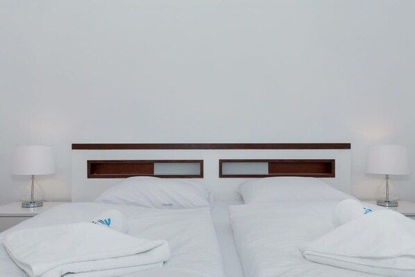 A hotel room with two single beds, each with a wooden headboard, white bedding, and a bedside table with a lamp.