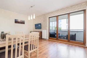 A dining area with a wooden table and chairs, a radiator, a television, and a sliding glass door leading to an outdoor balcony.