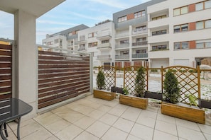 A balcony with a view of residential buildings, wooden planters with small trees, and a metal table.