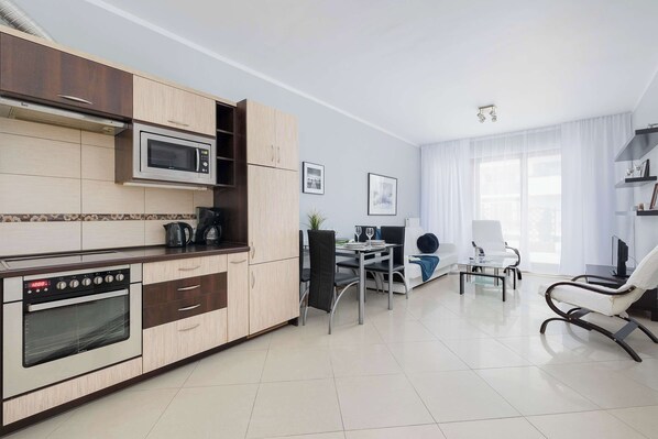 A modern kitchen with a microwave, oven, and wooden cabinets. There is a dining area with a table and chairs, and a seating area with a sofa and armchair.