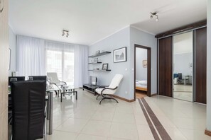 A modern living room with a dining area, a white chair, a TV, and a sliding door leading to a bedroom.
