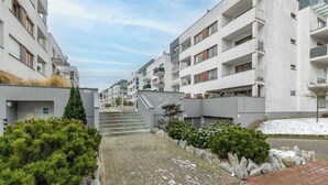 Ein Wohngebäude mit mehreren Balkonen, einer zentralen Treppe und einem kleinen Garten mit Steinen und Sträuchern.