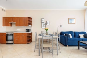 Una cucina moderna con mobili in legno, forno integrato e zona pranzo con un divano blu e un tavolo imbandito per quattro persone.
