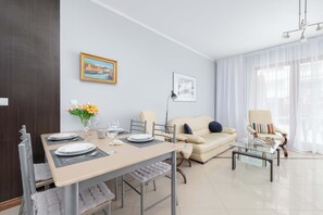 Un salon moderne comprenant un coin repas, un canapé, une table basse en verre et un tableau accroché au mur.
