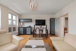 A modern living room with a sofa, a coffee table, a dining table with chairs, a flat-screen TV, and a cabinet.