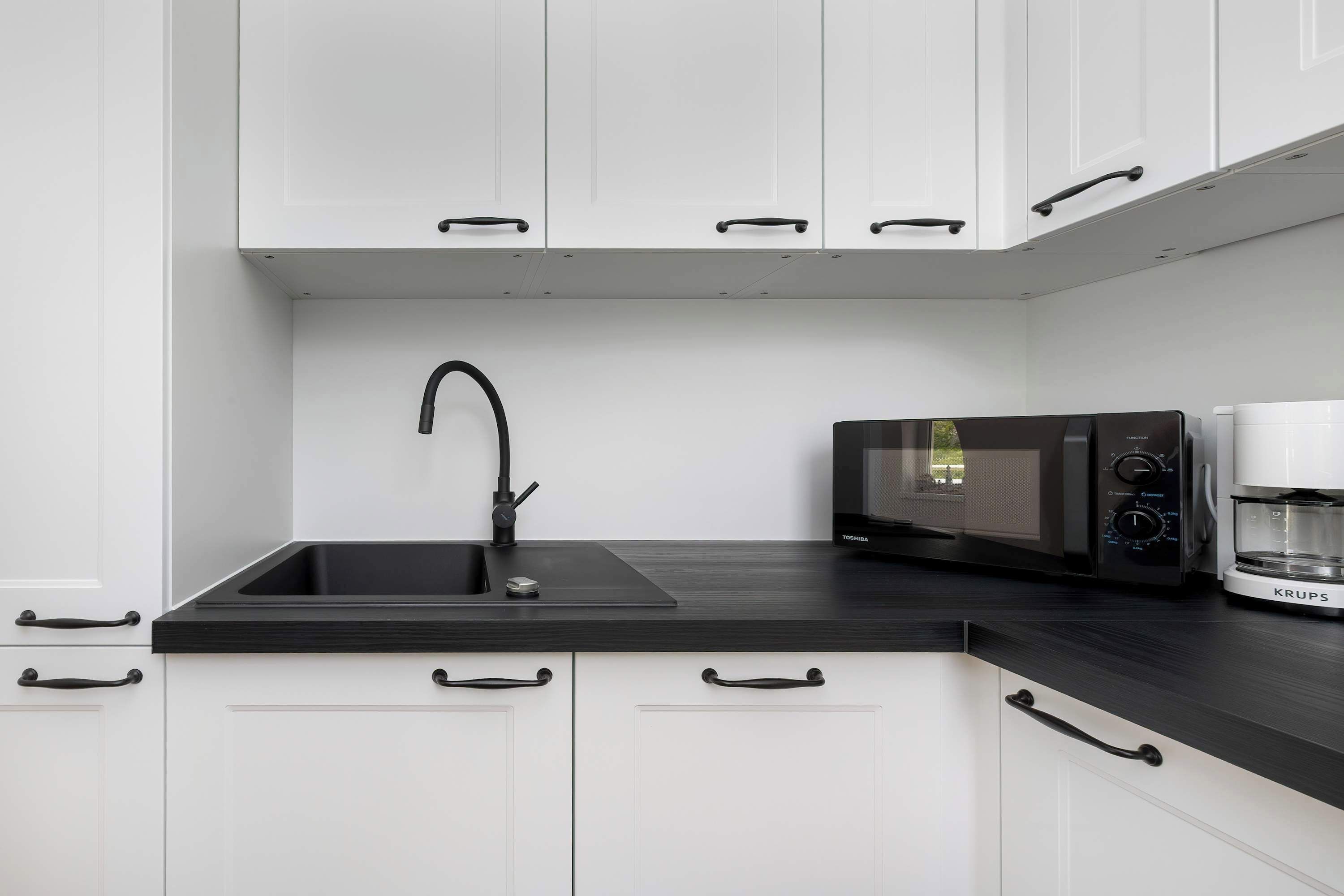 Een moderne keuken met witte kastjes, een zwart aanrecht, een spoelbak, een magnetron en een koffiezetapparaat.